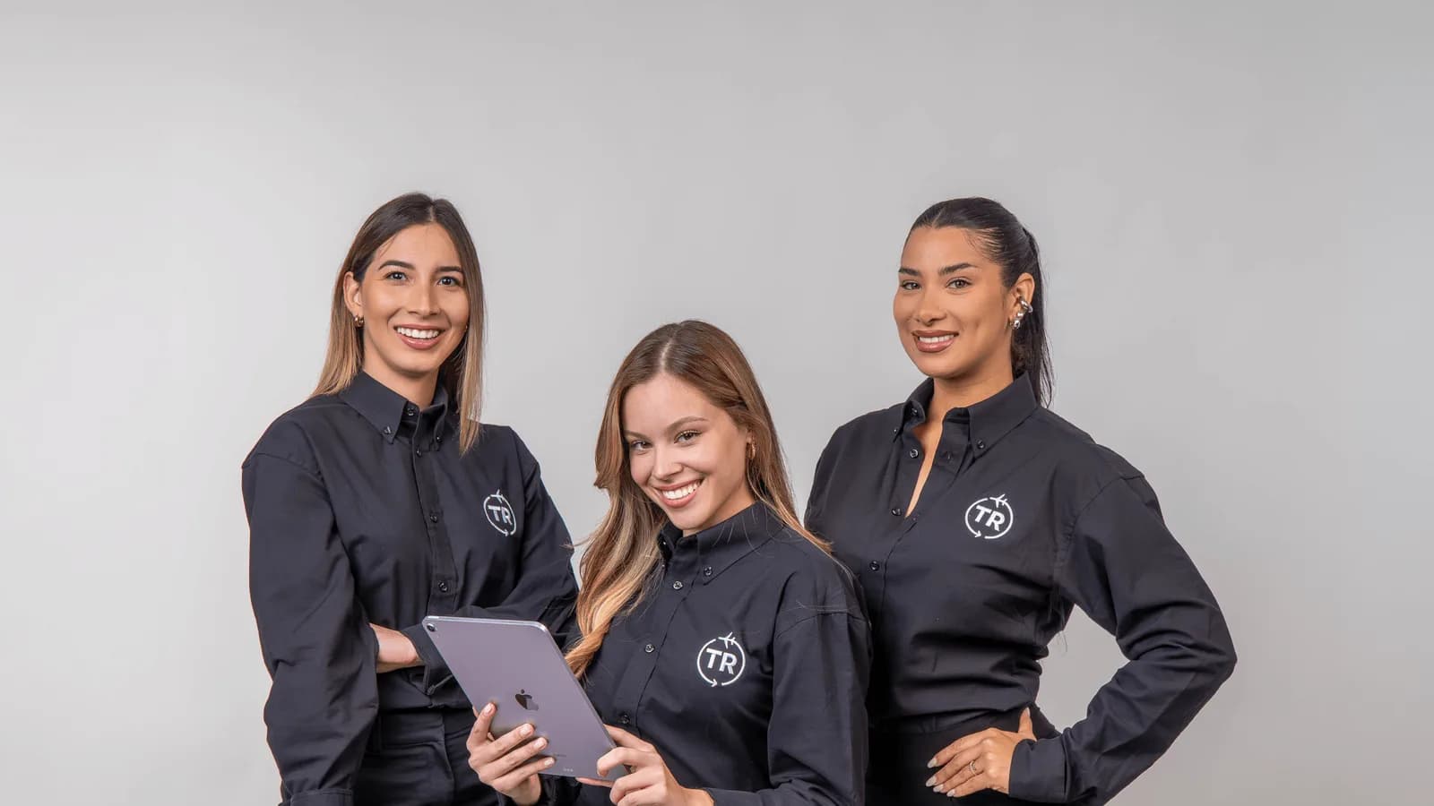Tres integrantes del equipo de Travel Remesas sonriendo con camisas de la marca, una de ellas con una tableta